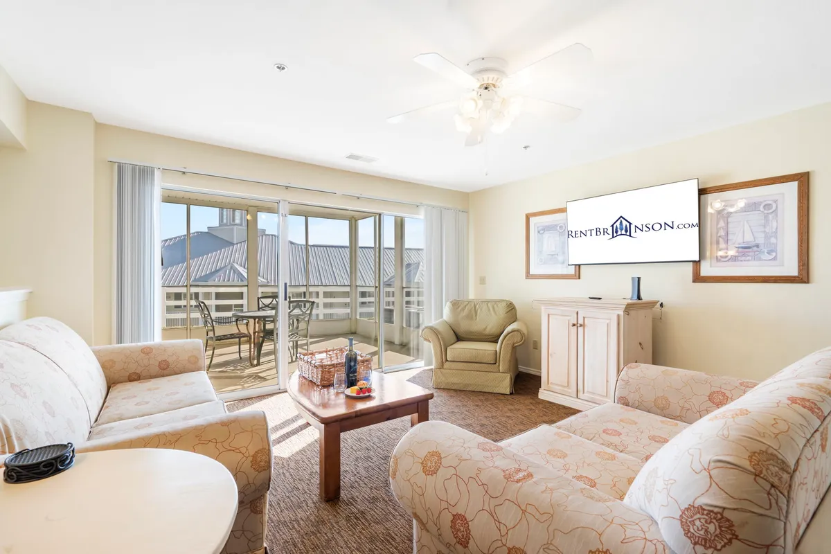 A living area with plush sofas, a coffee table, and a TV, flanked by sliding glass doors that lead to a patio with scenic views. The space is designed for cozy movie nights or stepping outside to catch a sunset.