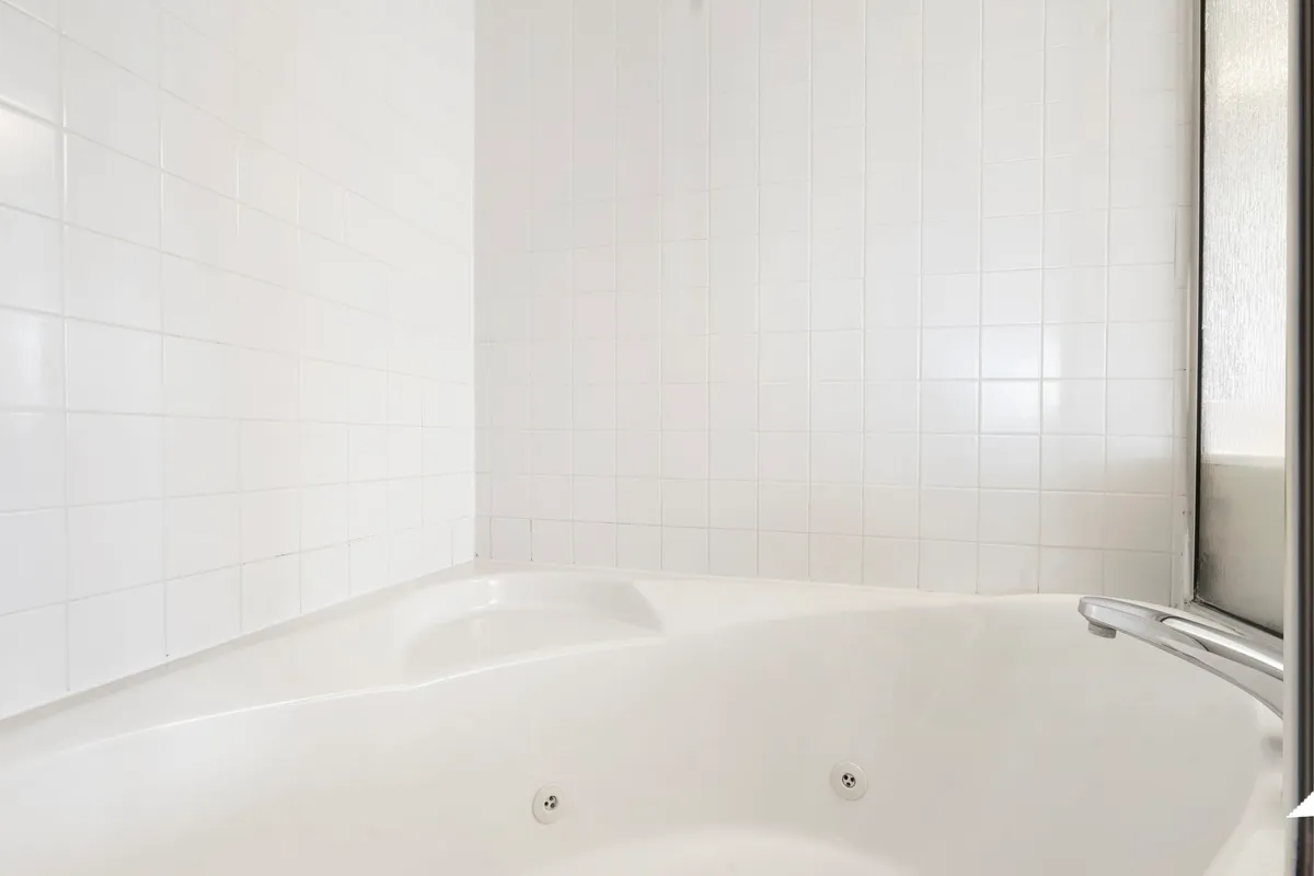 A luxurious ensuite bathroom with a jacuzzi soaker tub framed by pristine white tiled walls. The setting is minimalist with a spa-like feel, inviting guests to indulge in relaxation and self-care after an active day.