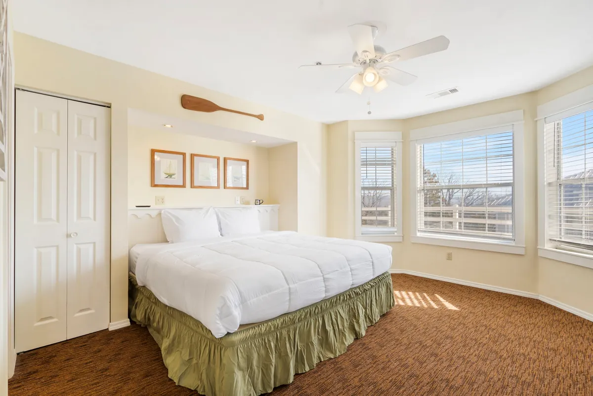 A serene bedroom with a plush king-sized bed dressed in white linens, enhanced by soft natural light streaming through a nearby window. Decorative elements like a paddle on the wall and framed artwork add a tranquil, personal touch. The atmosphere is peaceful and inviting, ideal for rest and rejuvenation.