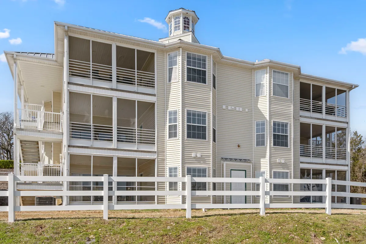 A three-story structure with a distinctive cupola stands amidst a fenced yard, featuring spacious porches and balconies. The welcoming exterior conveys ample outdoor space for both people and pets to enjoy.