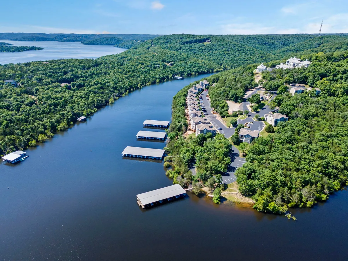 A tranquil exterior scene featuring a river, boathouses, lush greenery, and residential buildings. The natural setting suggests easy access to walking trails and the lakeshore, ideal for dog walks and outdoor exploration.