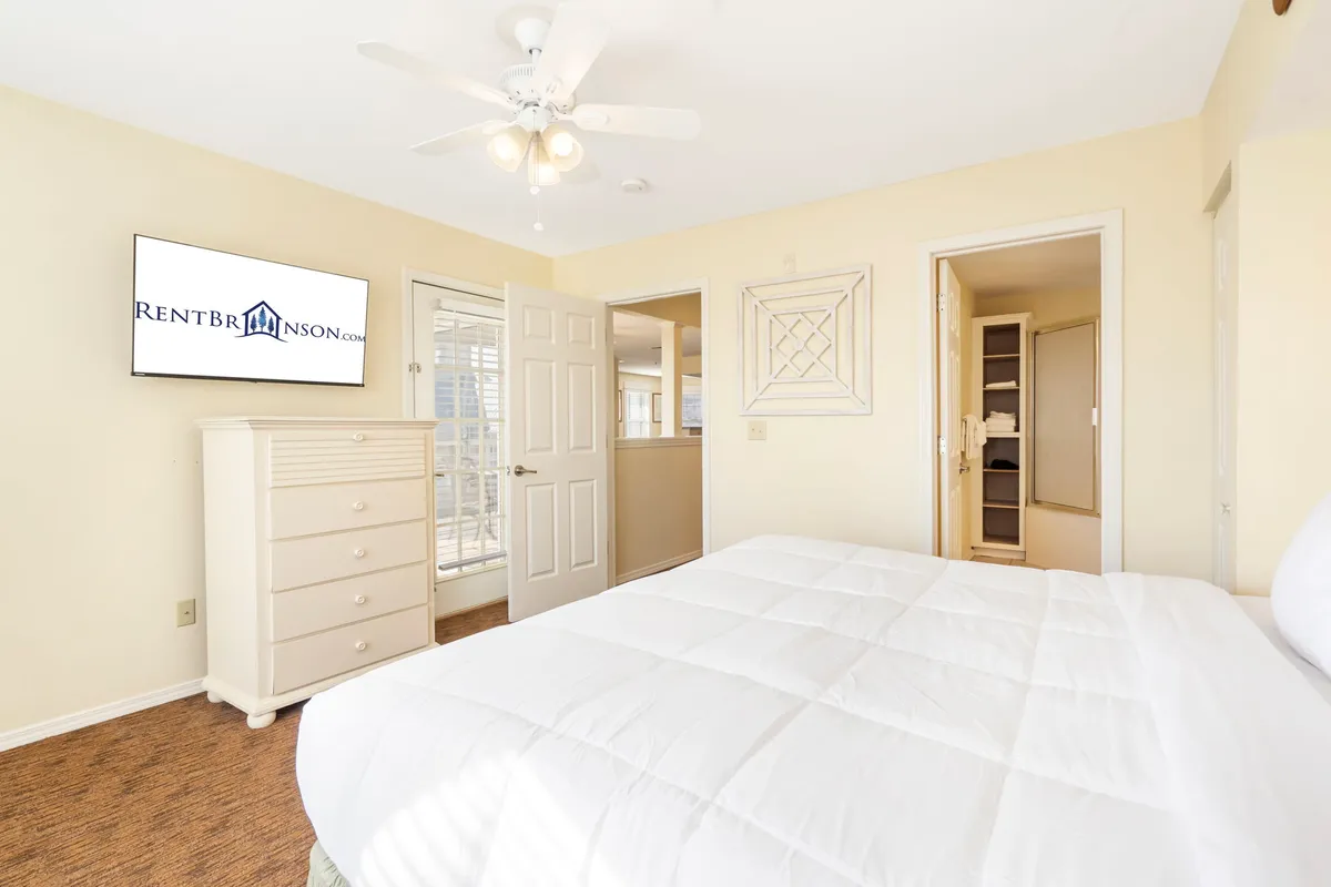 A cozy interior scene featuring a plush bed with white bedding, a dresser, and a wall-mounted TV, evoking a sense of comfort and relaxation. This space is ideal for families to unwind after an action-packed day, setting the stage for movie nights and quiet moments together.