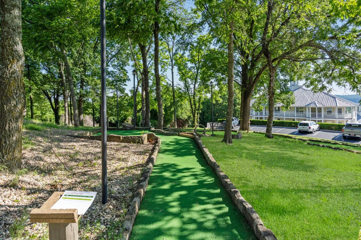 The photo focuses on a mini-golf pathway winding through lush trees with clear signage, inviting guests to partake in playful and social outdoor competition. The natural backdrop hints at the changing foliage across seasons.