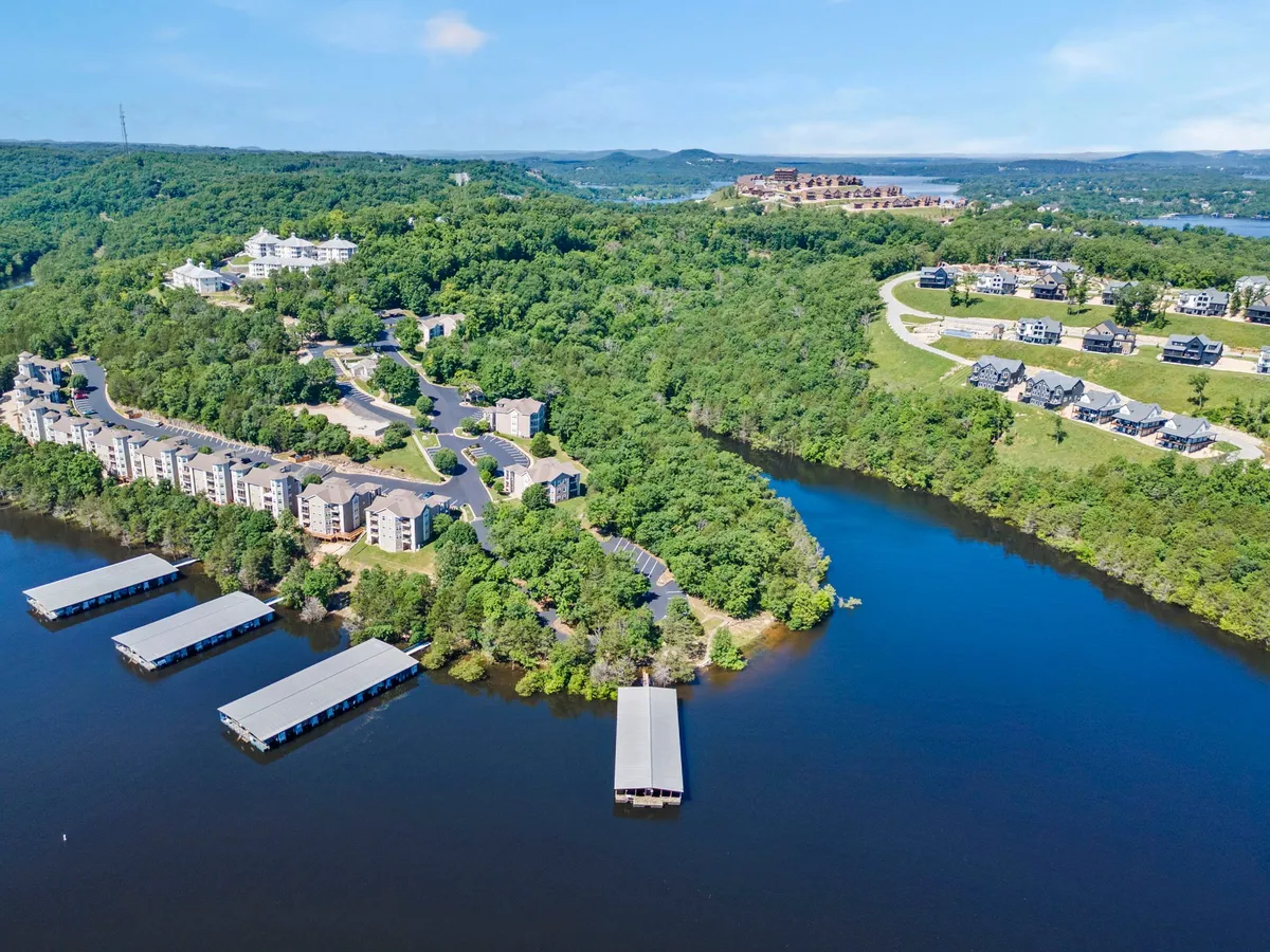 A panoramic view of the lake with docks, lush greenery, and residential complexes along the shore. The mood is tranquil, suggesting a lively lakeside community where guests can enjoy fishing, boating, and evening strolls by the water.