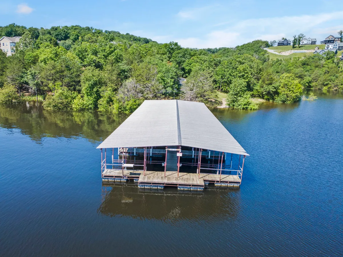 A peaceful boat dock stretches over calm water, framed by trees on the shore. The tranquil setting hints at early morning fishing, boat launches, and serene lakefront relaxation.